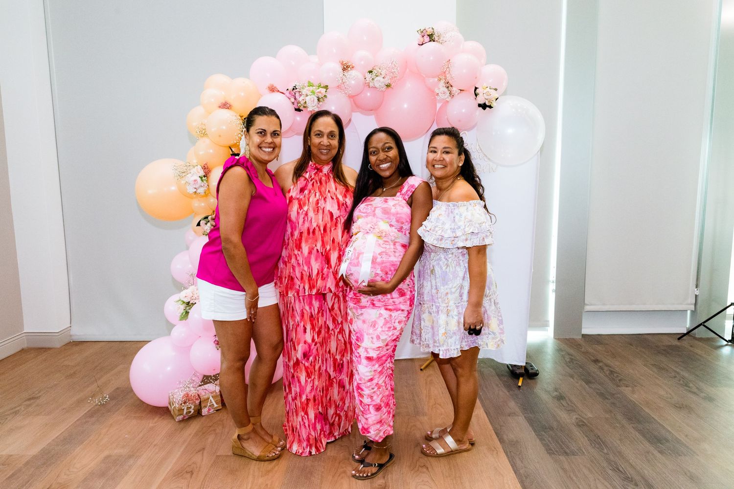 Four people pose together in front of a pink balloon arch at a festive celebration.
