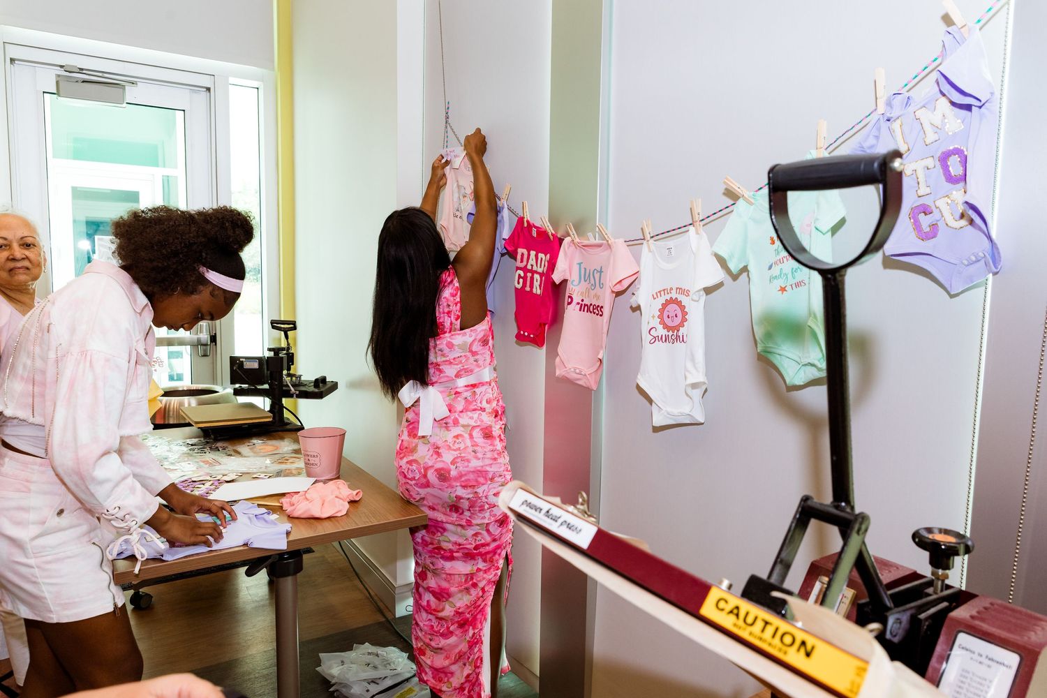 People gathered in a medical waiting room with equipment and pink decorations visible.