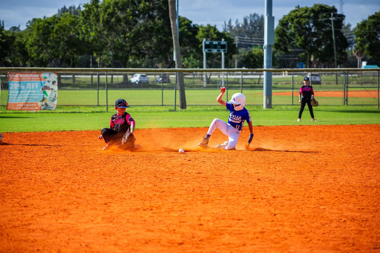 Baseball players practicing on a sunny day at a field with bright orange clay infield and green grass outfield.