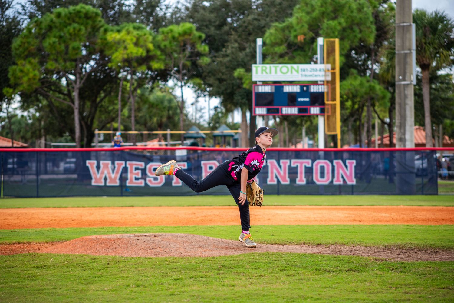 Baseball field with 'WEST BOYNTON' text visible on outfield wall during a game.