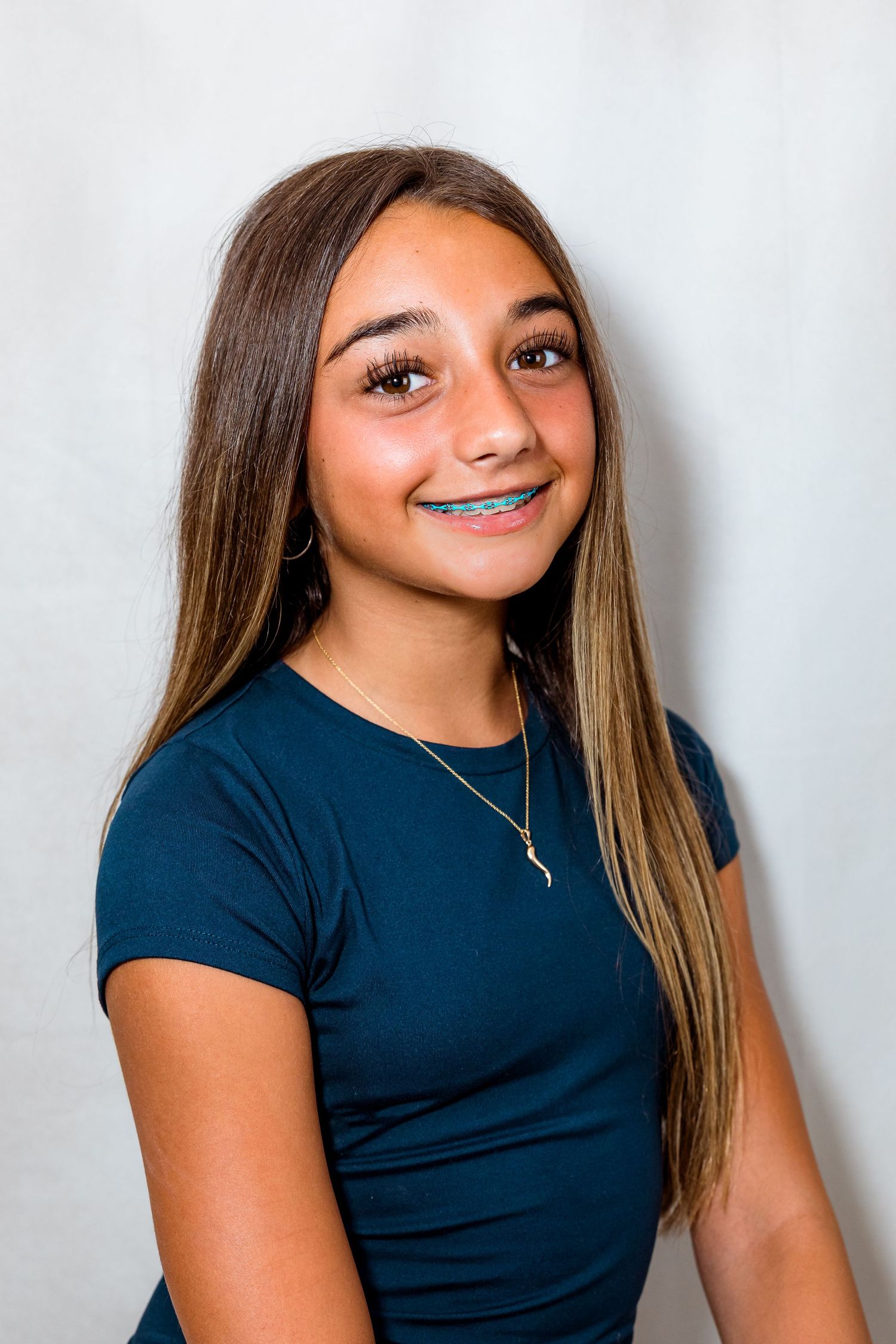Smiling teenage girl with long brown hair, braces, and a blue shirt poses for a portrait photo.