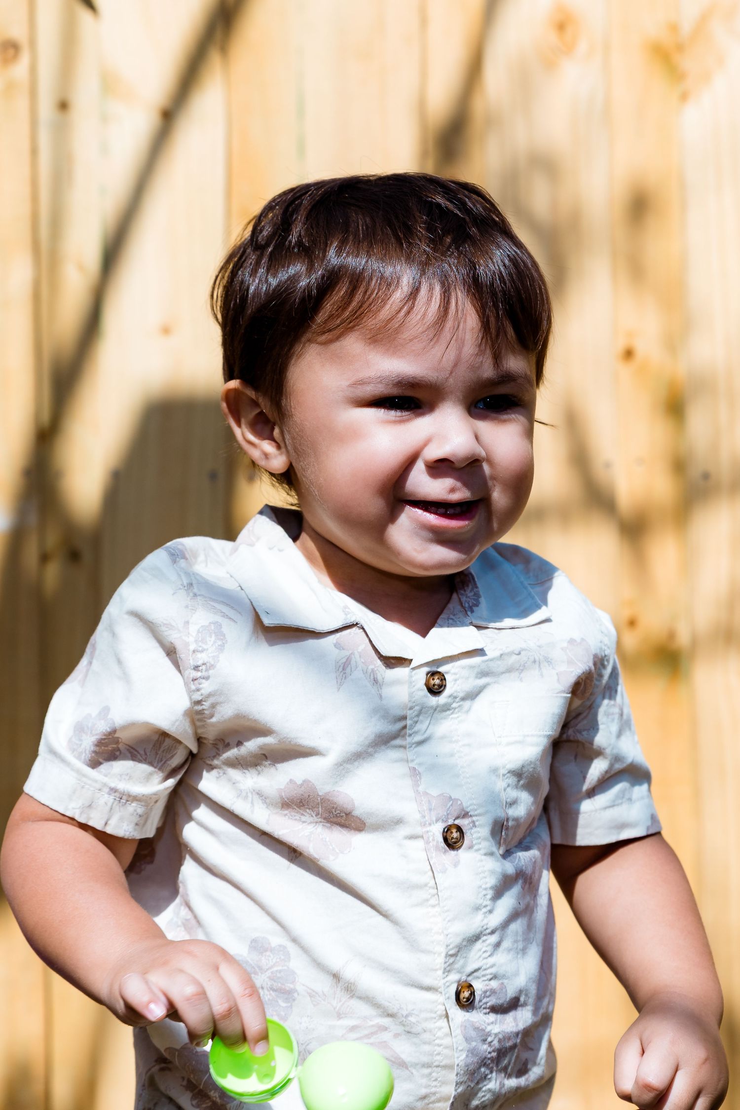 Toddler in a white button-down shirt smiling and playing outdoors on a sunny day.