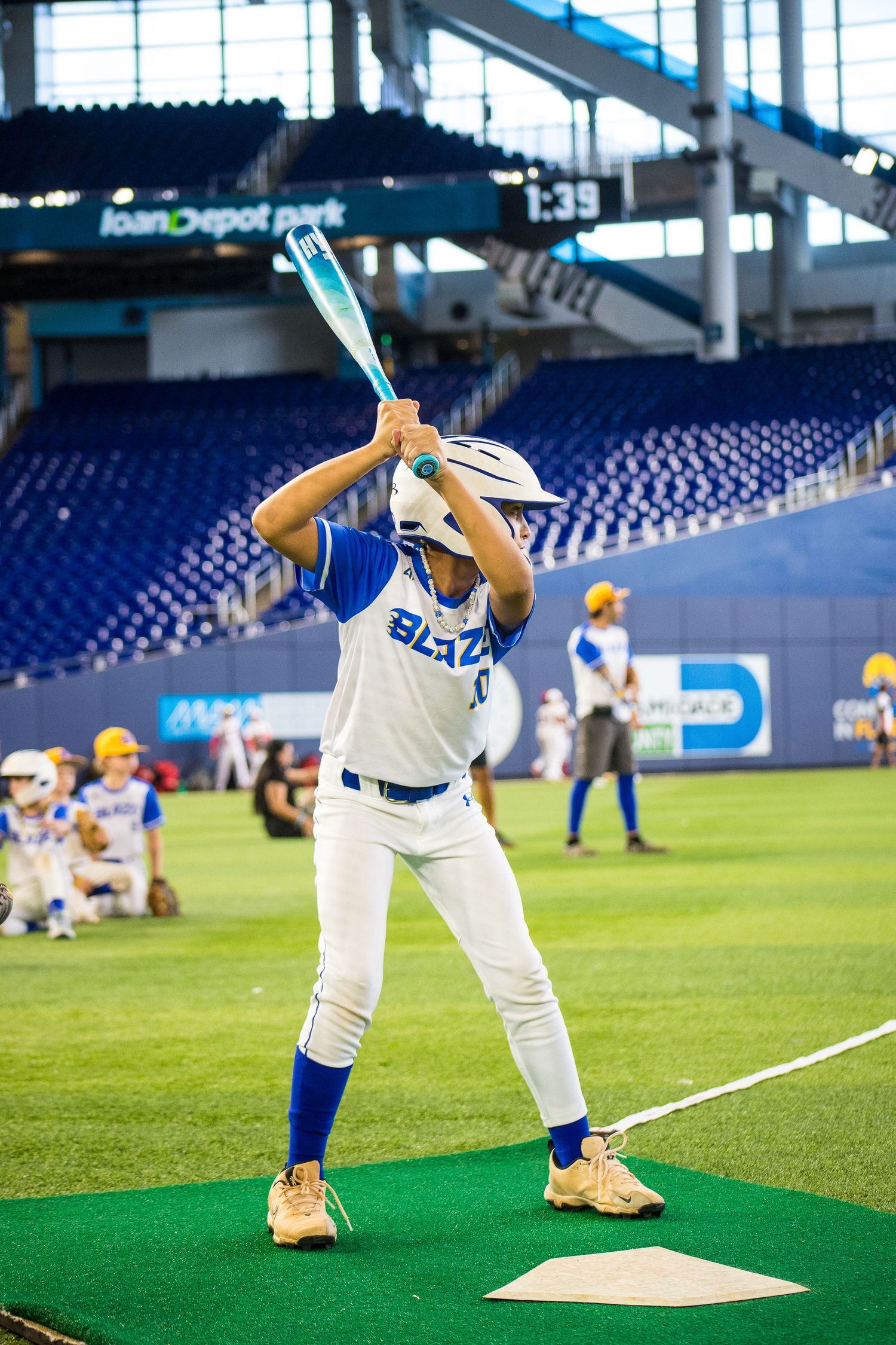 Baseball player in white uniform taking practice swings at home plate in empty stadium.