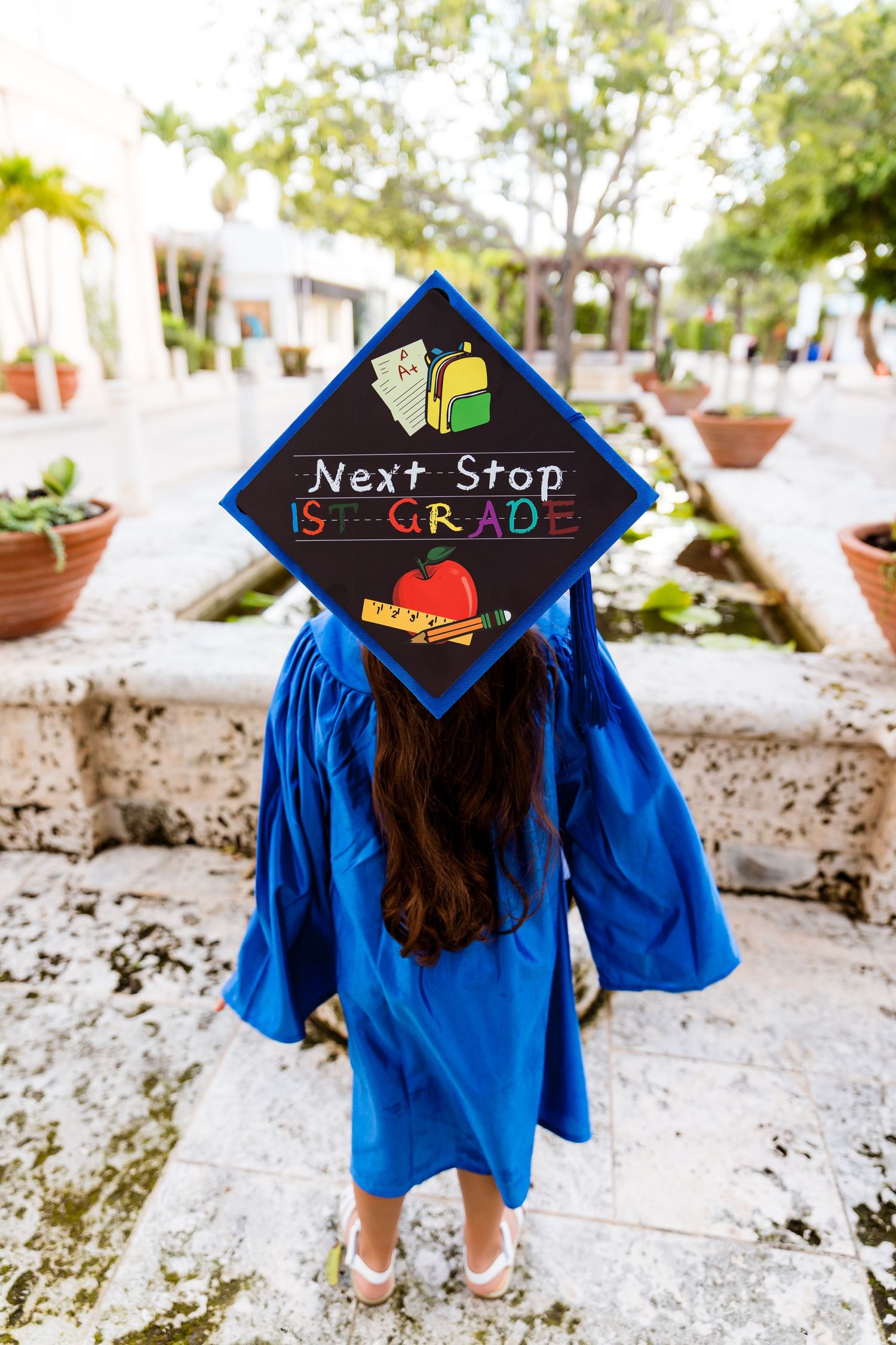 Graduate wearing blue cap and gown with decorated mortarboard reading 'Next Stop 5th Grade' in colorful design.