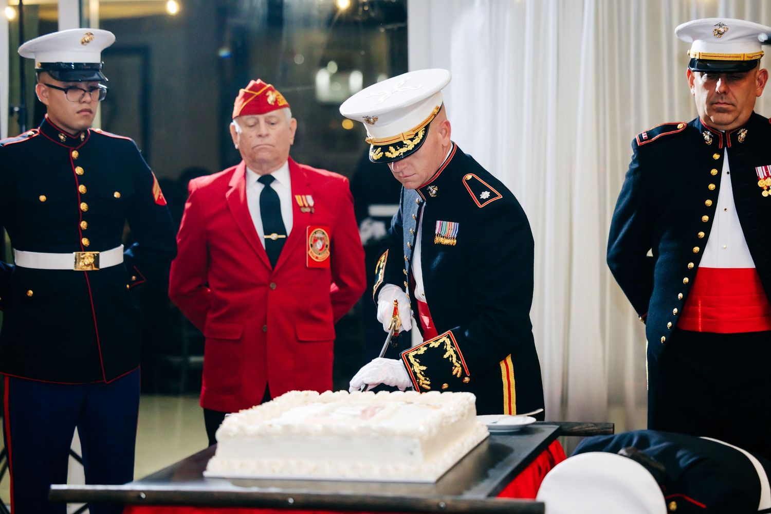 Military service members in dress uniforms and red jackets gather at a formal event.
