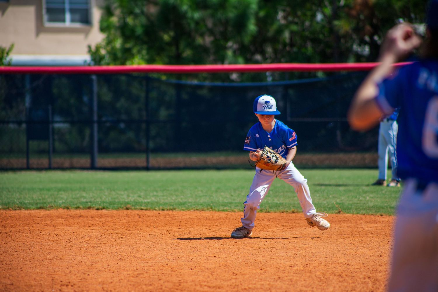 A baseball player crouches in fielding position on the infield dirt during a game.