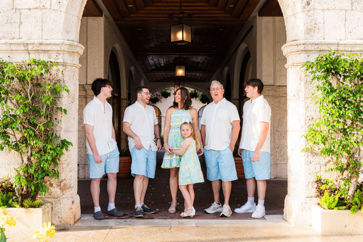 A group poses in matching blue and mint green attire under an elegant stone archway with hanging lanterns.