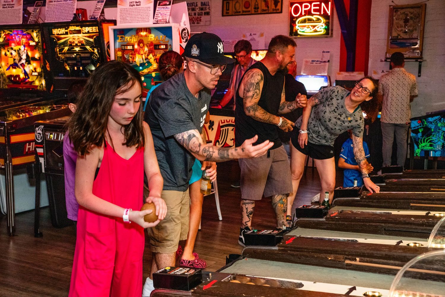 A group of people, including a woman in a red dress, standing in an arcade or entertainment venue.