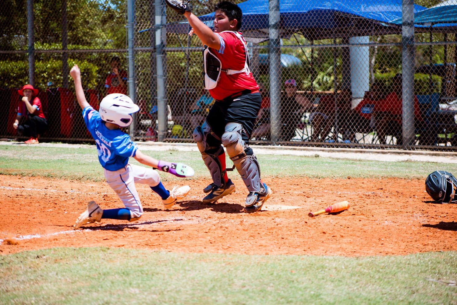 Baseball player sliding into home plate while catcher attempts to make the tag during youth game.