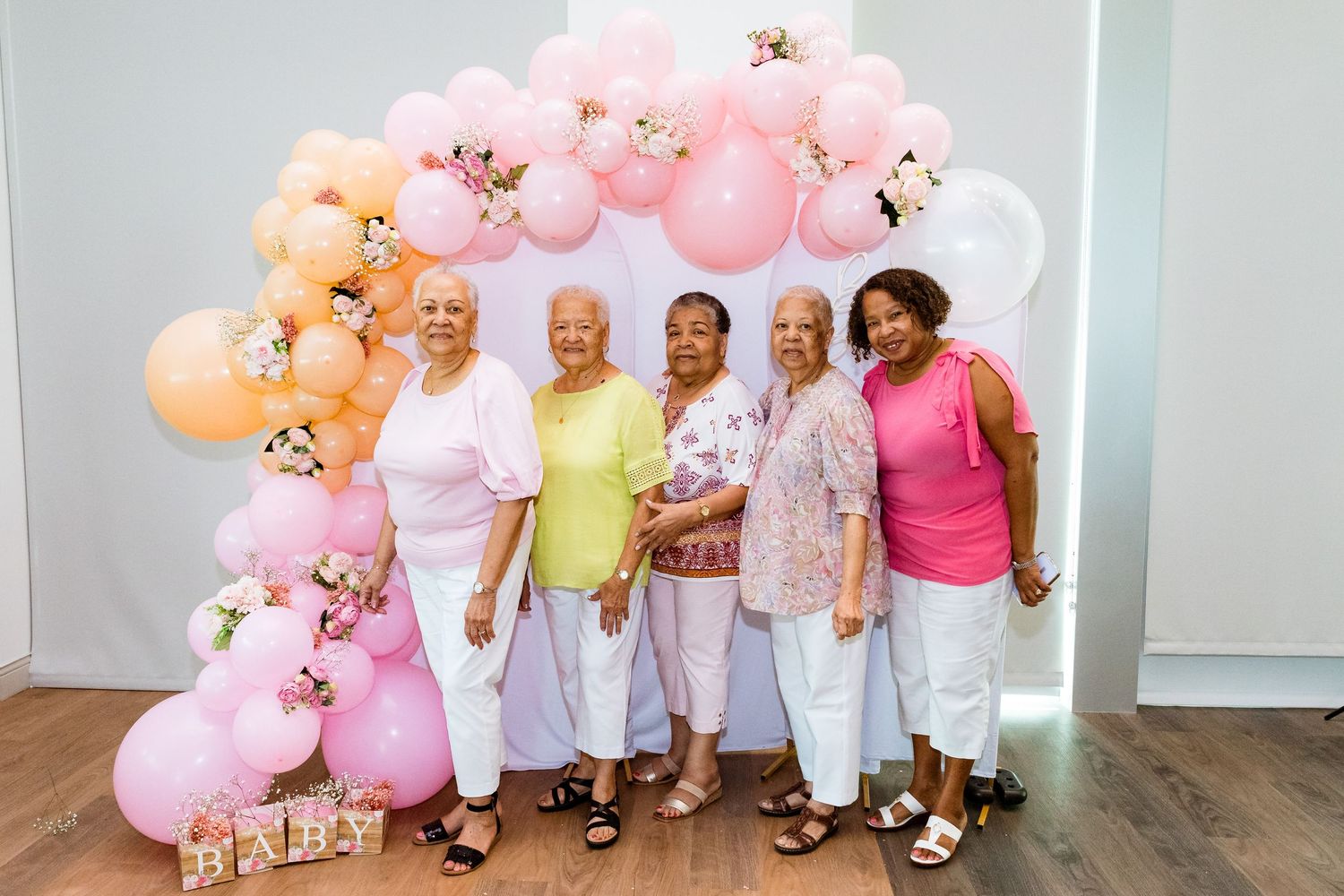 A group posing in front of a pink balloon arch at a celebration.