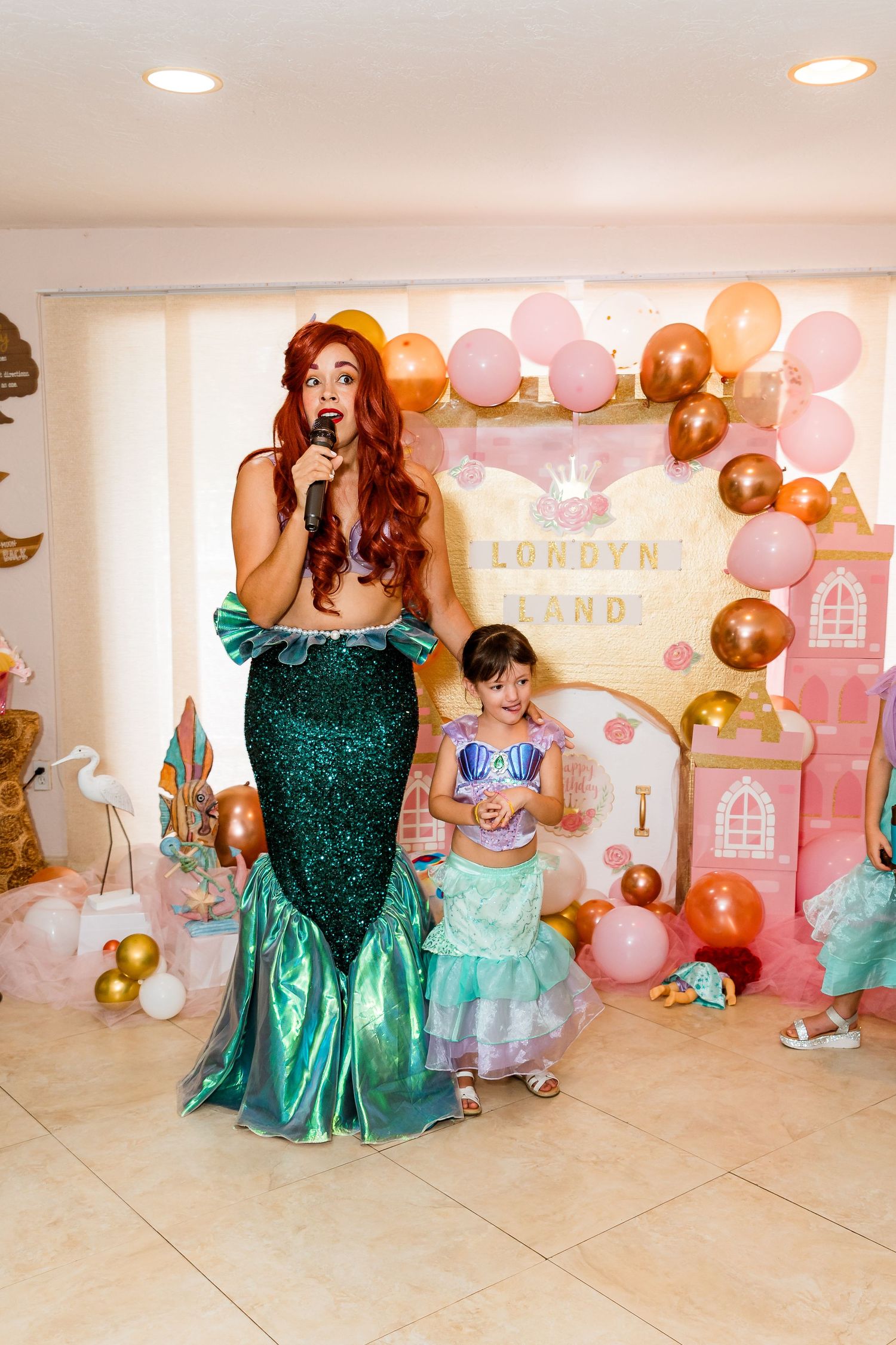 Mermaid themed birthday party setup with balloons, decorations and performers in sparkly green costumes.