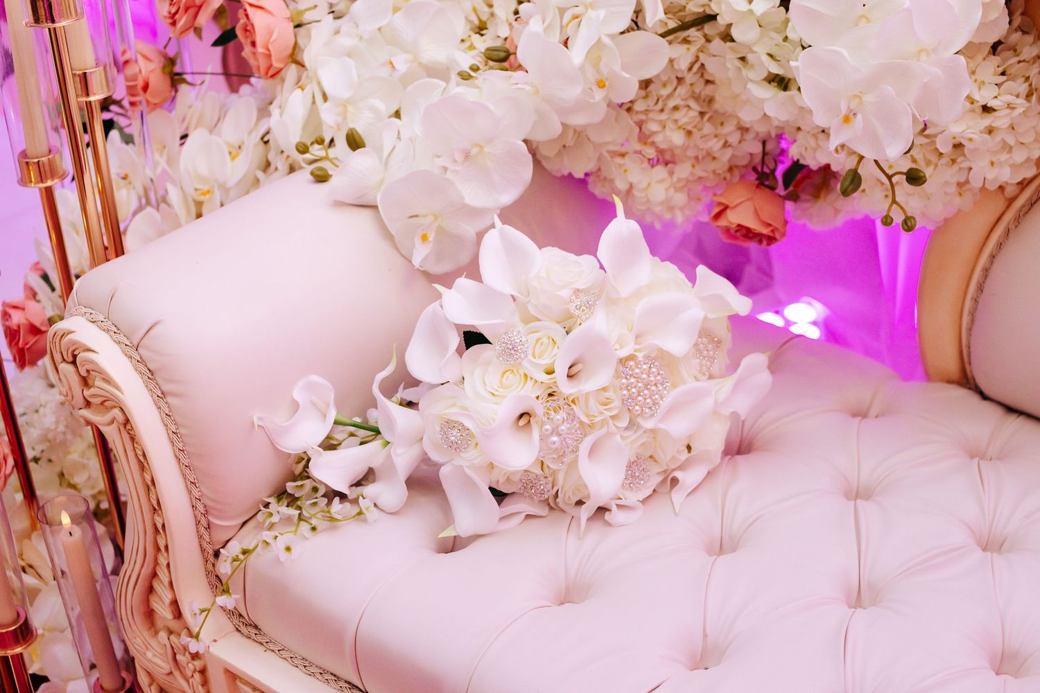 Elegant white floral arrangements and decor with soft pink lighting create a romantic wedding reception atmosphere.