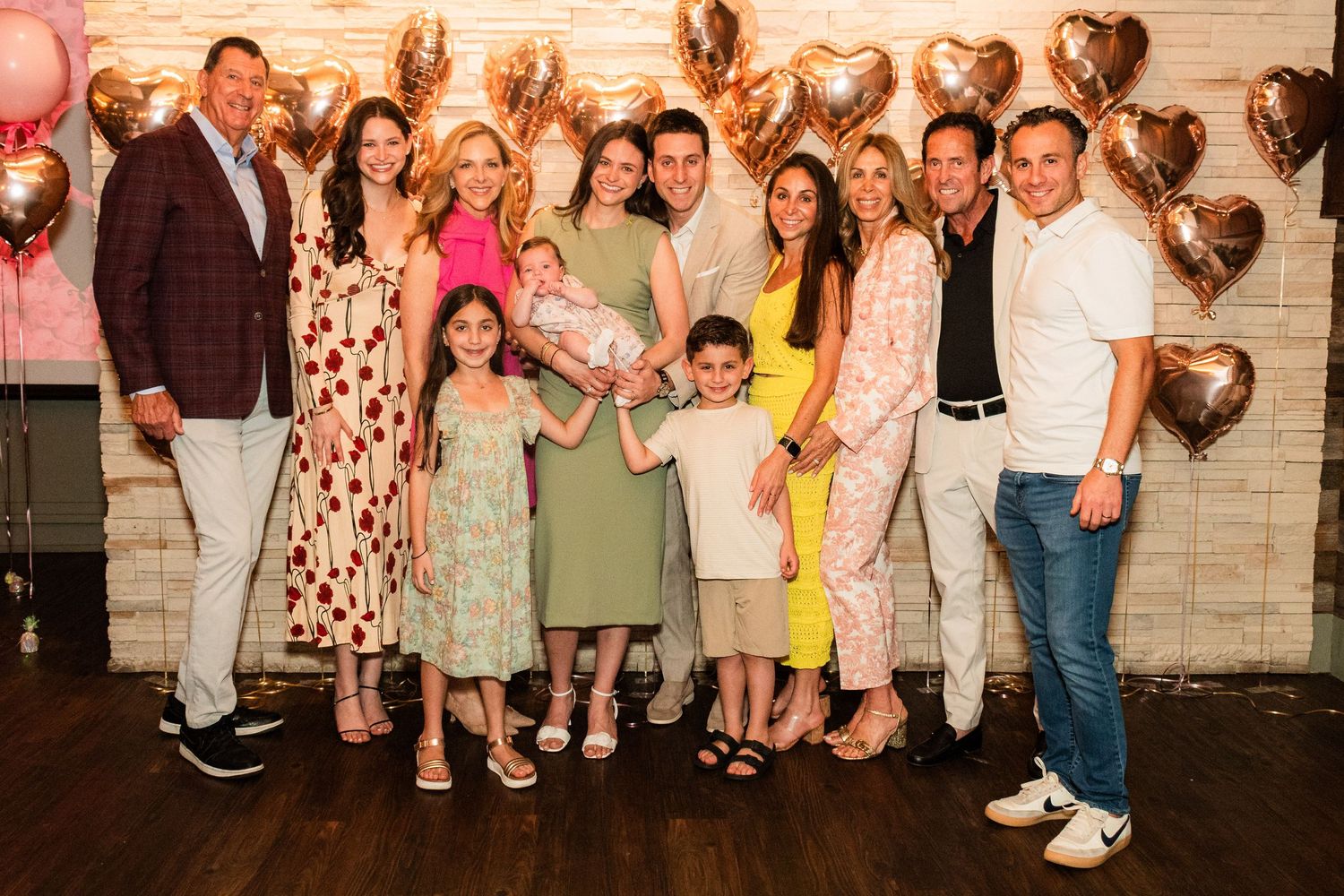 A celebration gathering with a group of people posing in front of a wall decorated with metallic heart balloons.