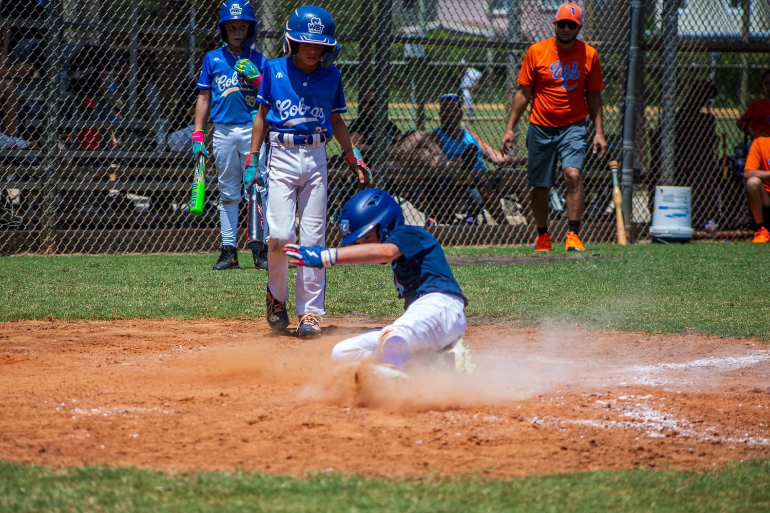A baseball player slides into home plate creating a cloud of dust during an intense play at the plate.