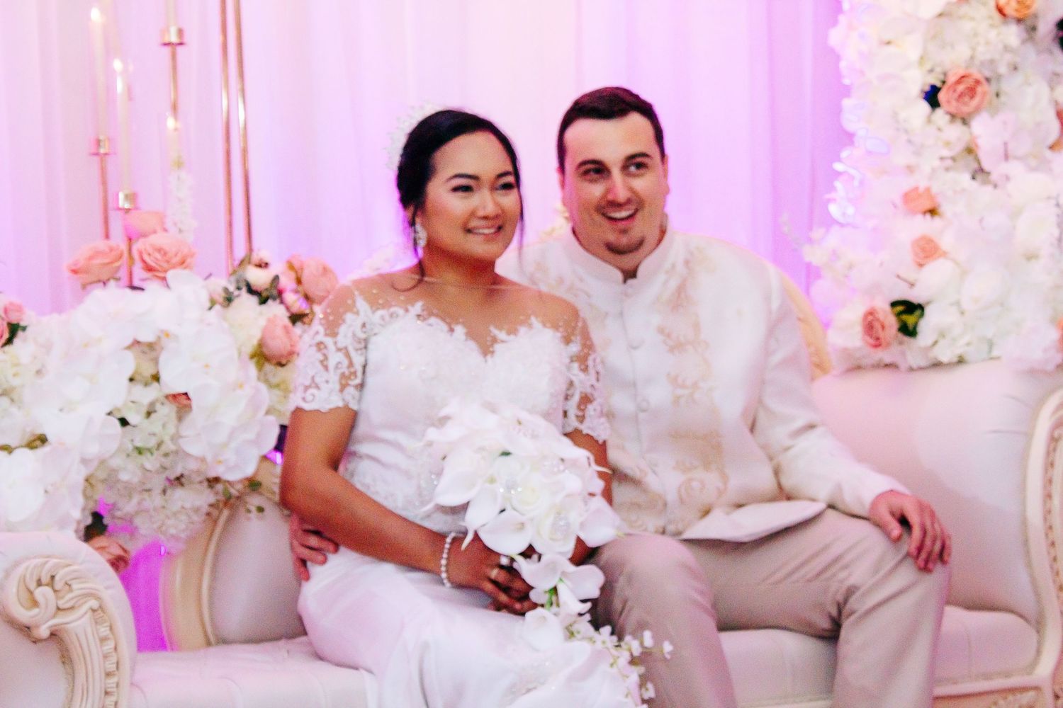 Wedding reception venue decorated in pink lighting with white floral centerpieces and elegant table settings.