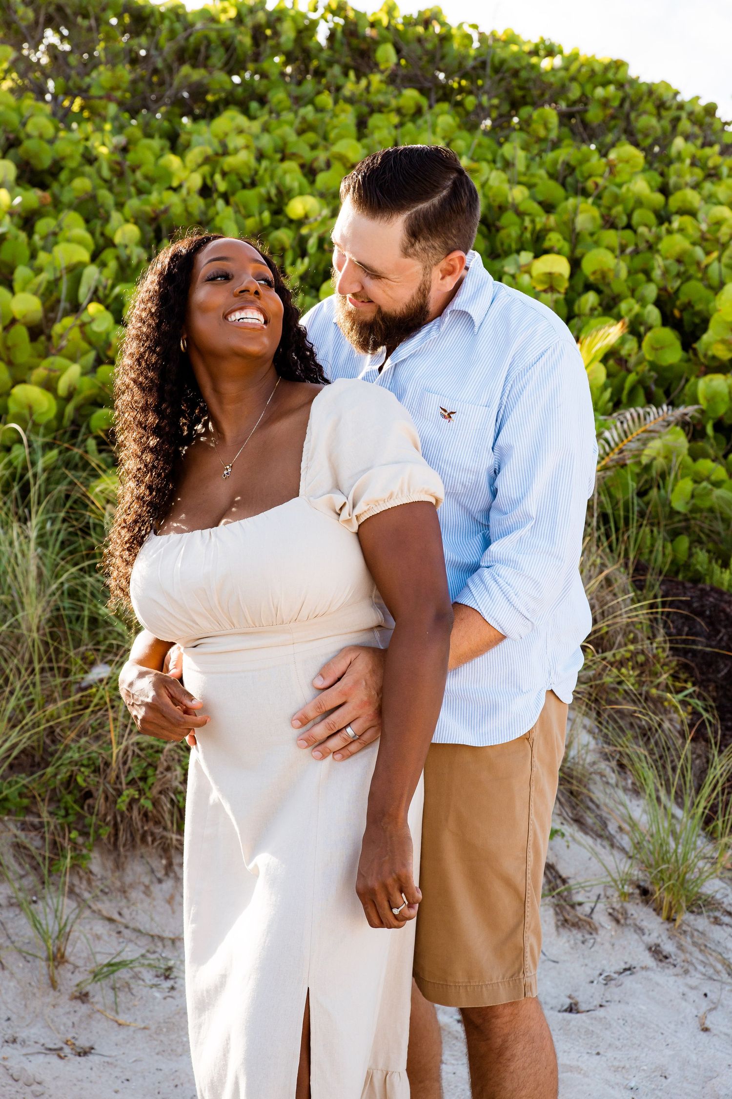 A couple shares romantic moments together against a beachside backdrop of sea grapes and sand dunes.
