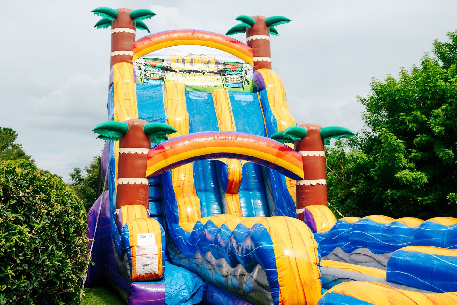Large inflatable waterslide with palm tree decorations and bright orange and blue colors.