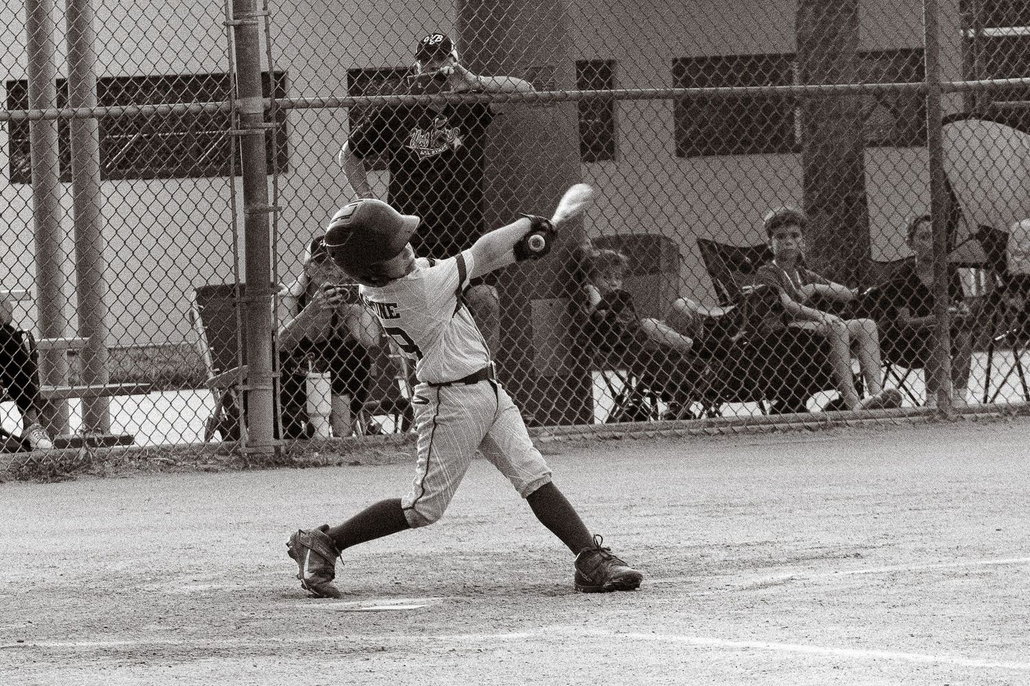 Black and white photo of youth baseball player mid-swing during baseball game.