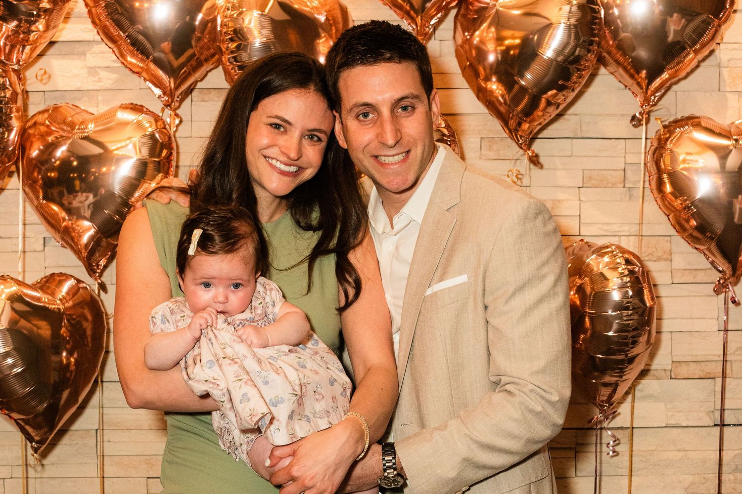 Family portrait with rose gold heart balloons decorating a brick wall background.