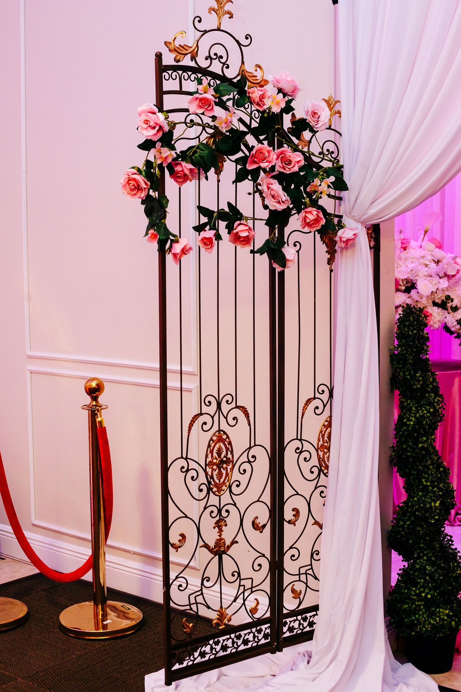 Decorative wrought iron gate adorned with climbing pink roses and white draping.