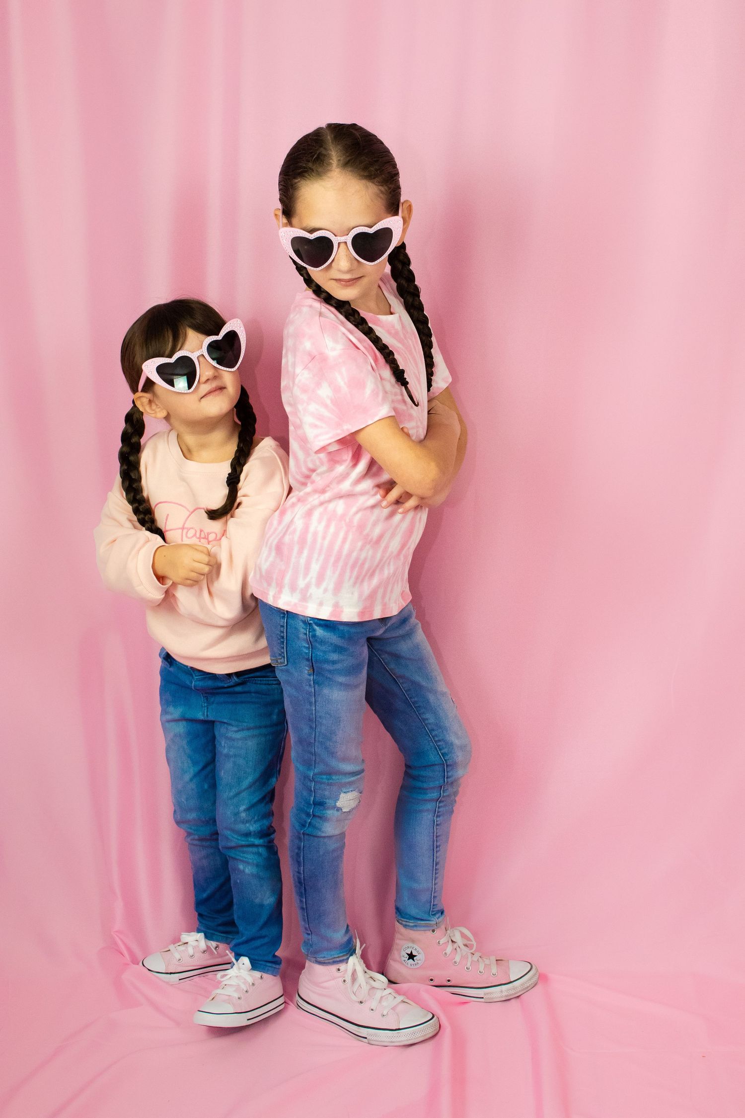 Two children in matching outfits strike cool poses wearing heart-shaped sunglasses.