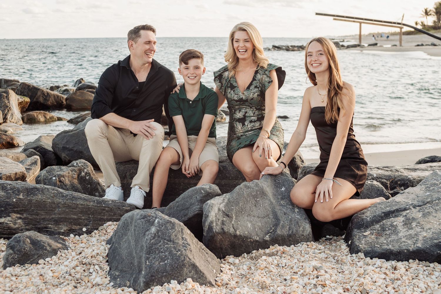 Family sits casually on rocky beach during sunset photoshoot.