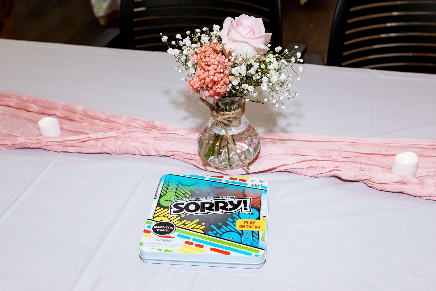Pink and coral flower centerpiece in a vase with Sorry board game on a white tablecloth.
