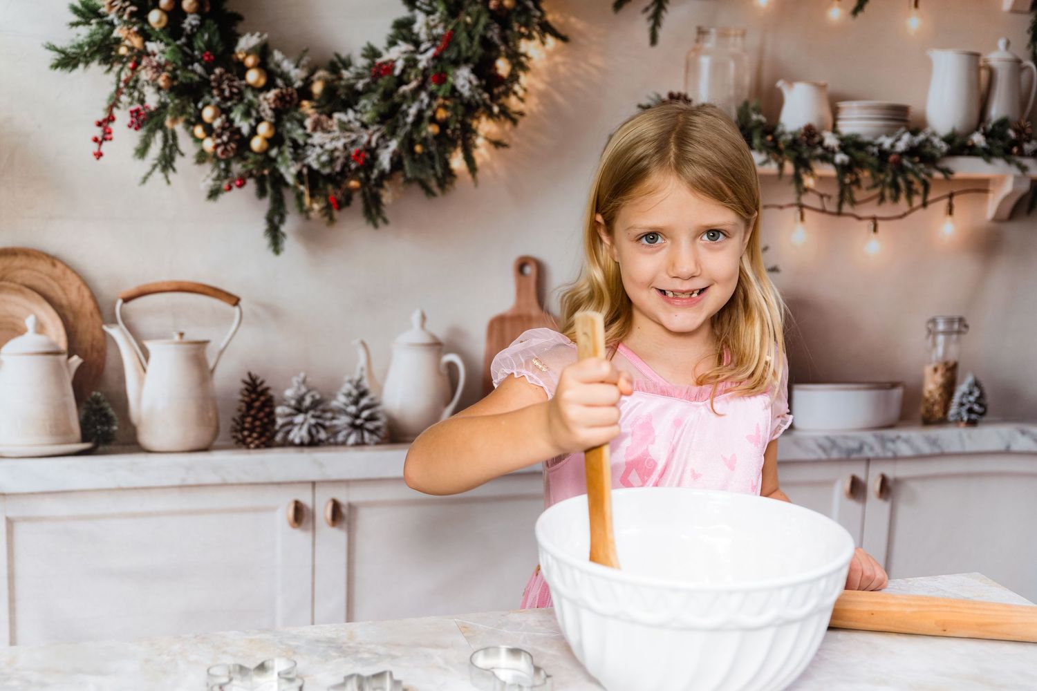 Person in red sweater standing in kitchen with white cabinets and holiday greenery decorations.