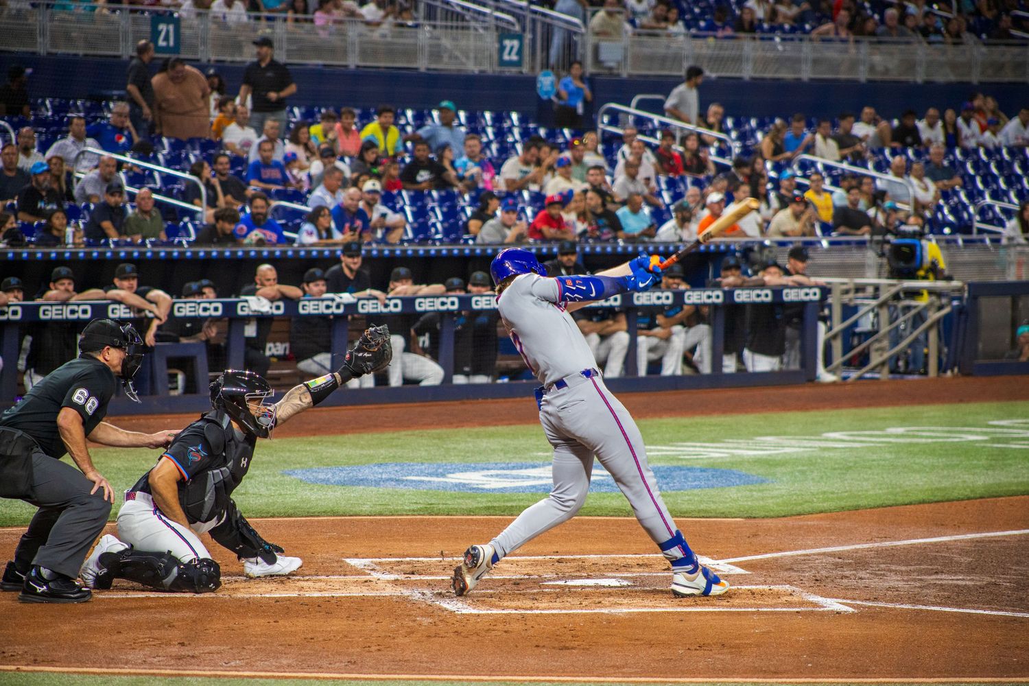Baseball player slides into home plate during intense game action at a stadium with crowd in background.