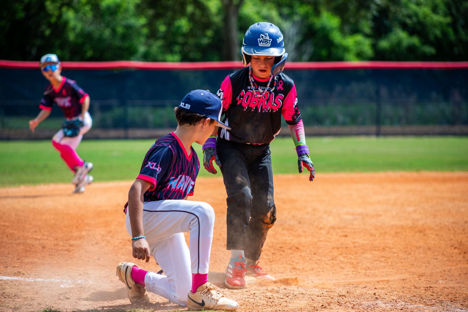 A softball player slides into base during a competitive game on a dirt infield.