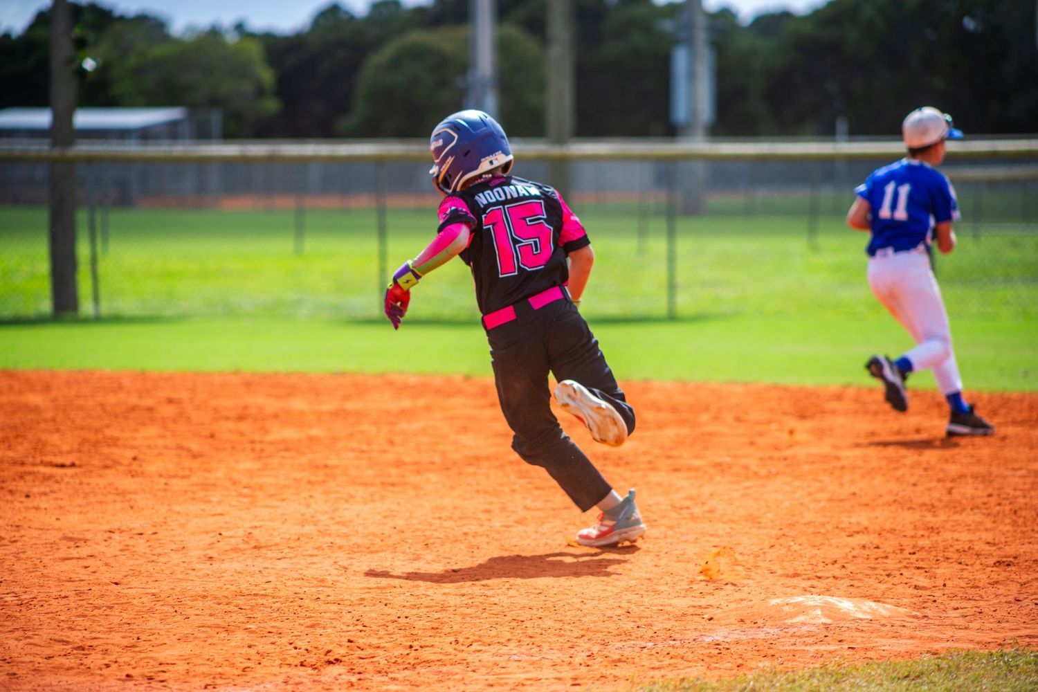 Youth baseball players practice fielding drills on an orange clay infield during a sunny afternoon practice session.