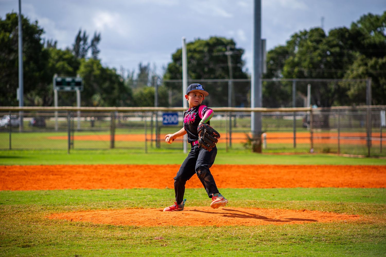 Baseball player sliding into base during game on dirt infield of sunny baseball diamond.