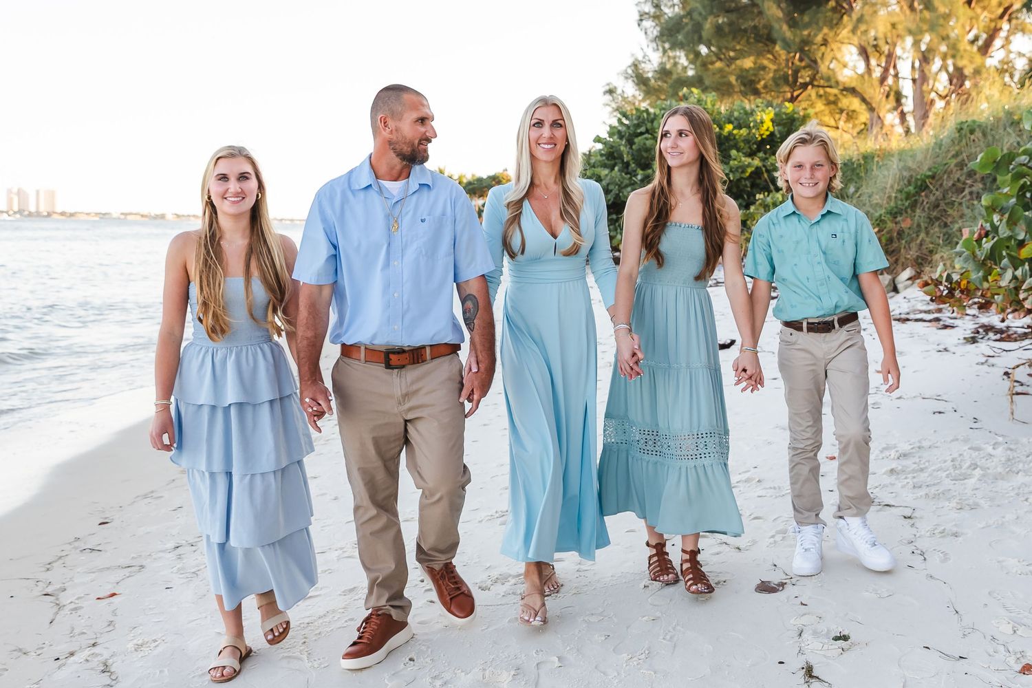 Family walking together on beach wearing coordinated blue and white coastal outfits.