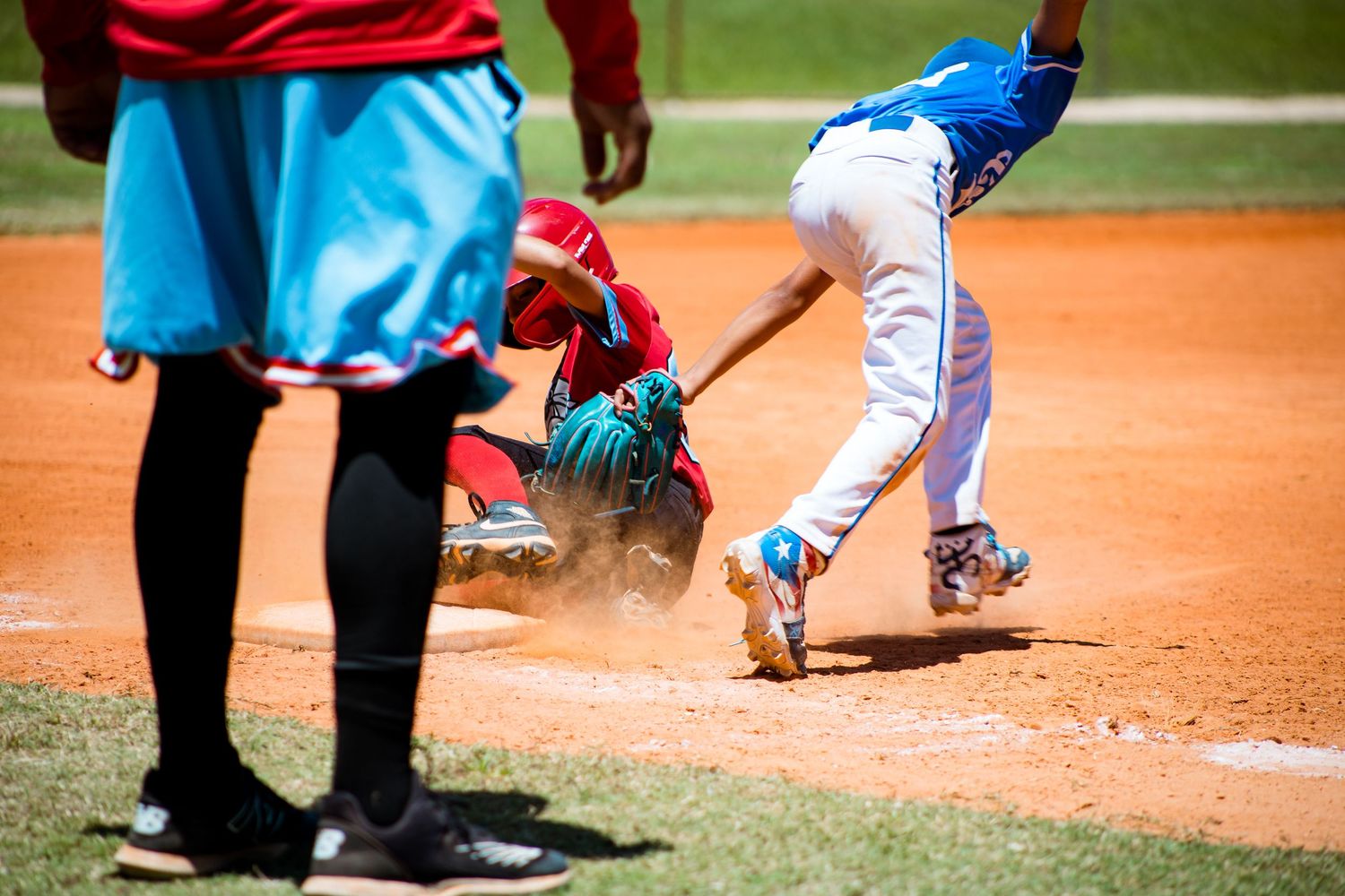 Baseball player slides into home plate creating dust cloud during intense play.