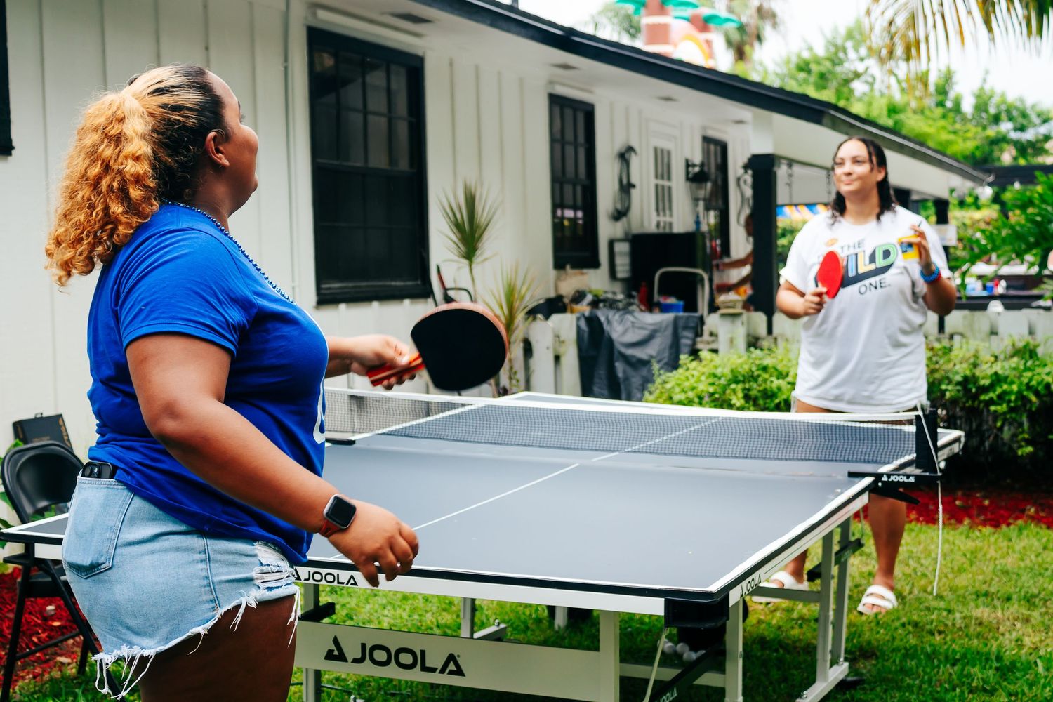 Group playing table tennis on multiple outdoor ping pong tables.