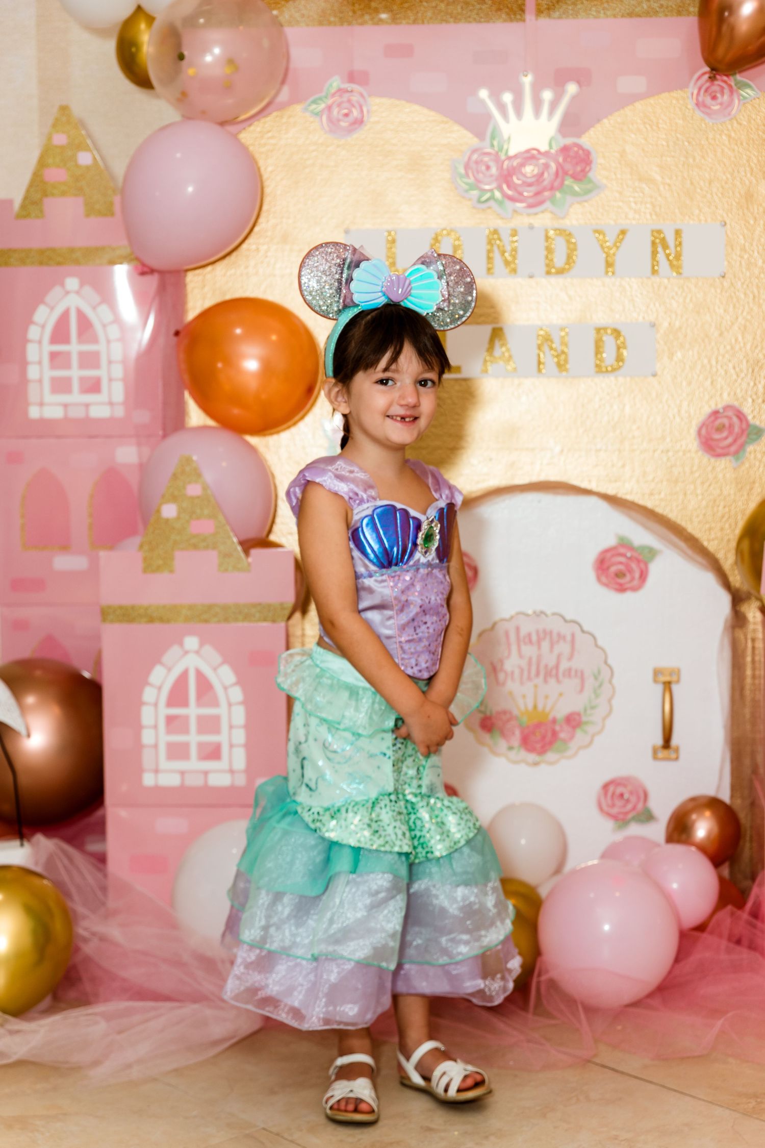 Pink princess castle themed party backdrop with balloons in gold, pink and rose colors against a pastel wall.