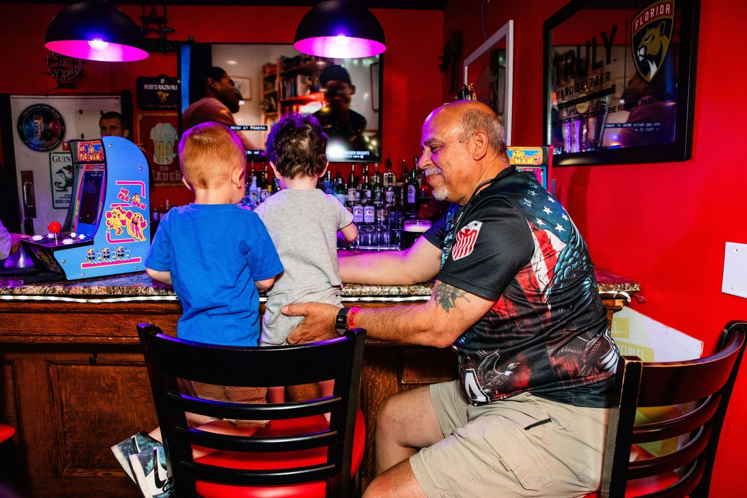 A lively bar scene with patrons seated at a counter and tables, surrounded by colorful decor and lighting.