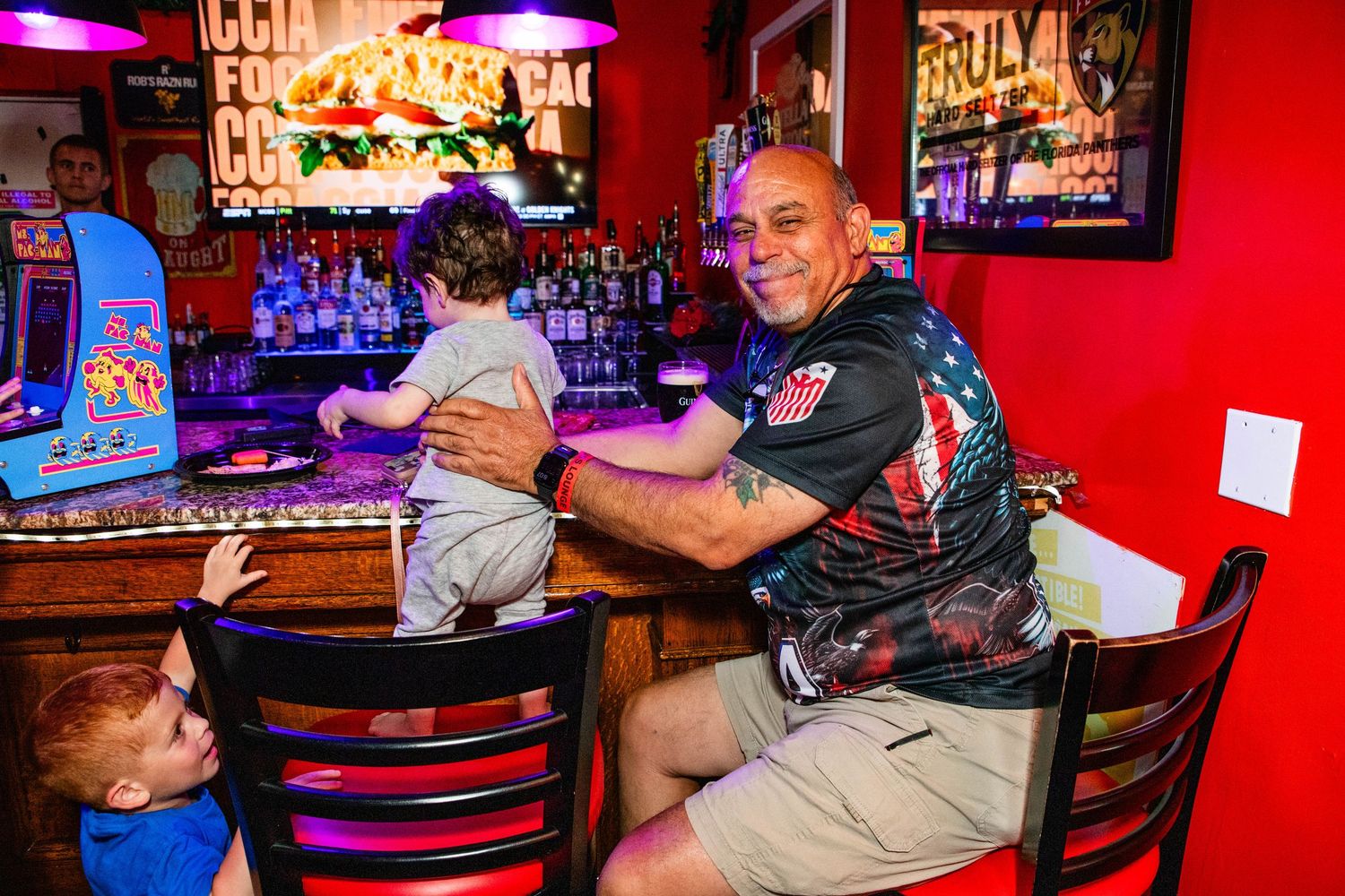 Two men enjoying drinks at a bar with arcade games in the background.