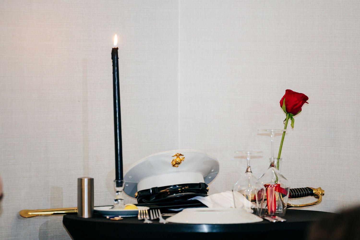 Simple white table setting at a wedding reception with a single red rose in a glass vase.