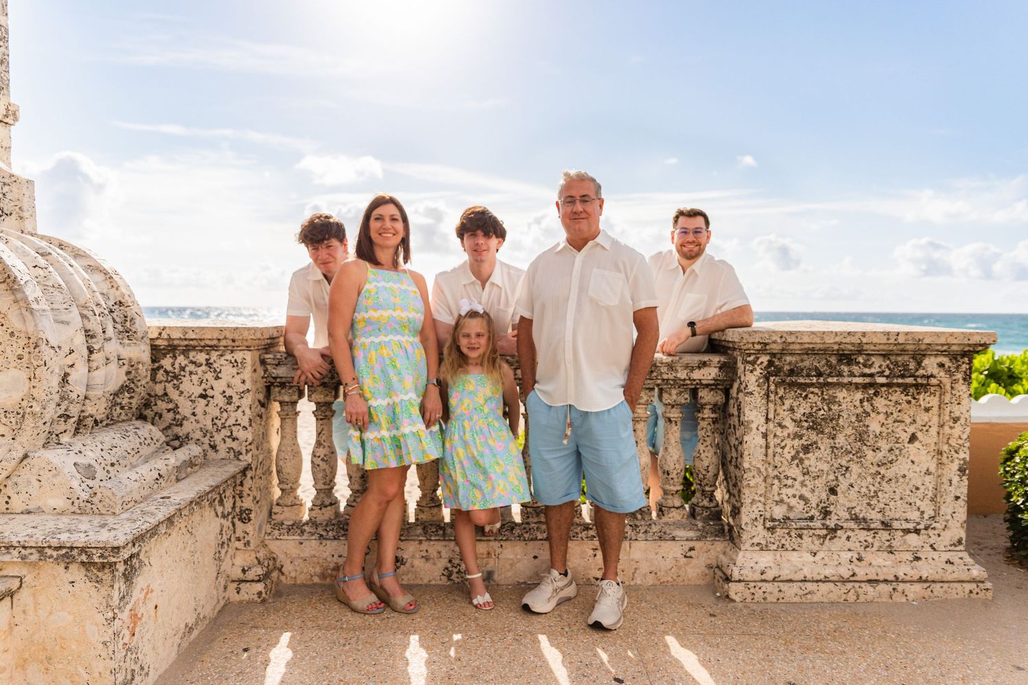 A group poses together on a stone balcony overlooking a scenic coastal view on a sunny day.