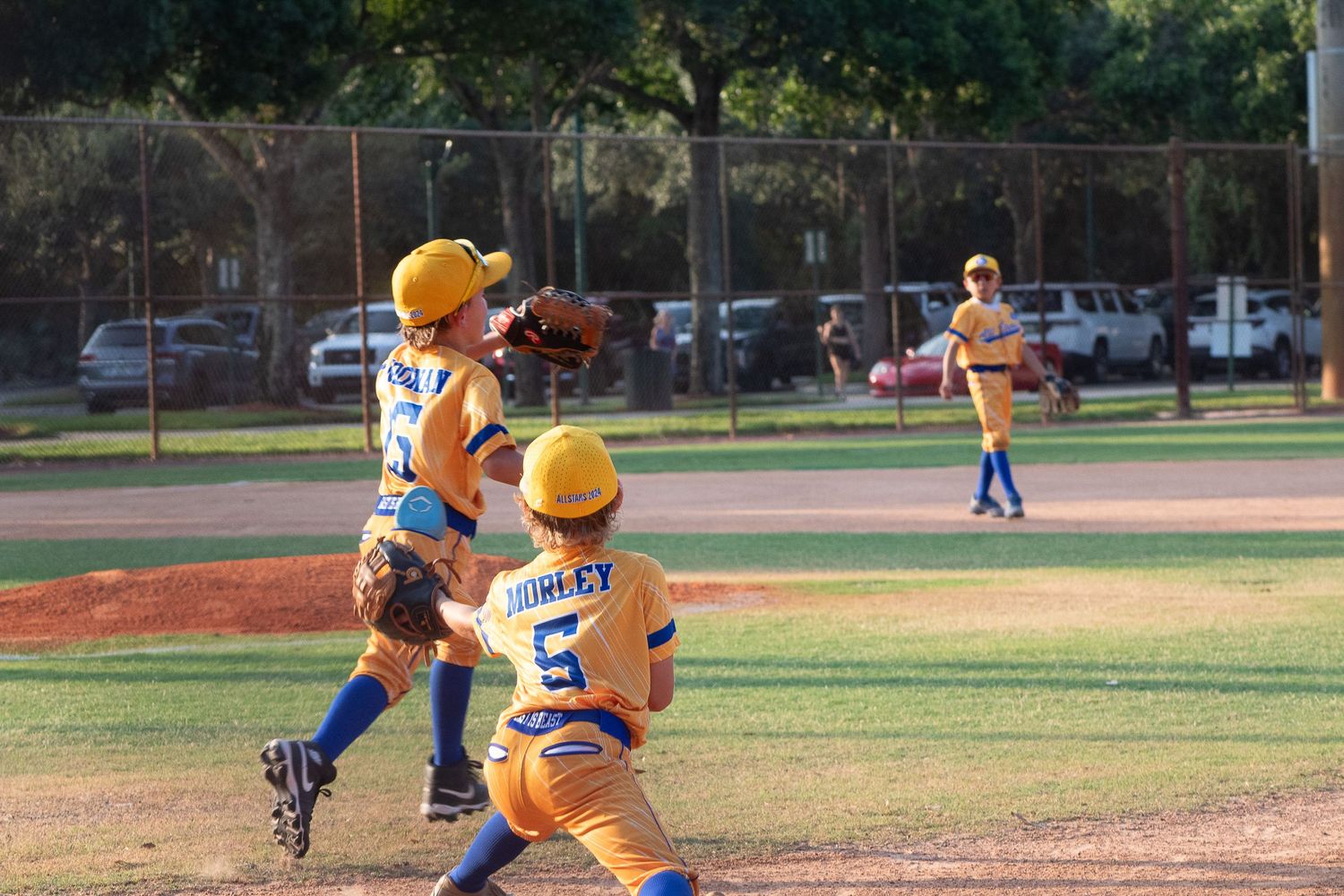 Youth baseball players in yellow uniforms positioned on the field during a game.