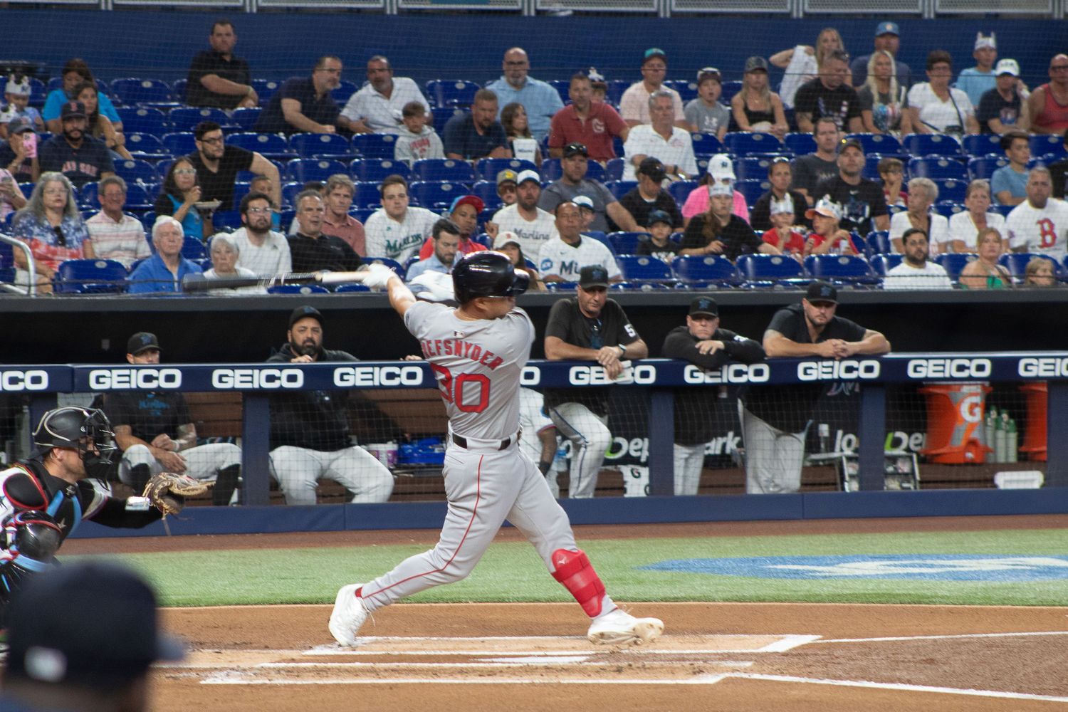 A batter follows through on their swing during a baseball game with fans in the background.