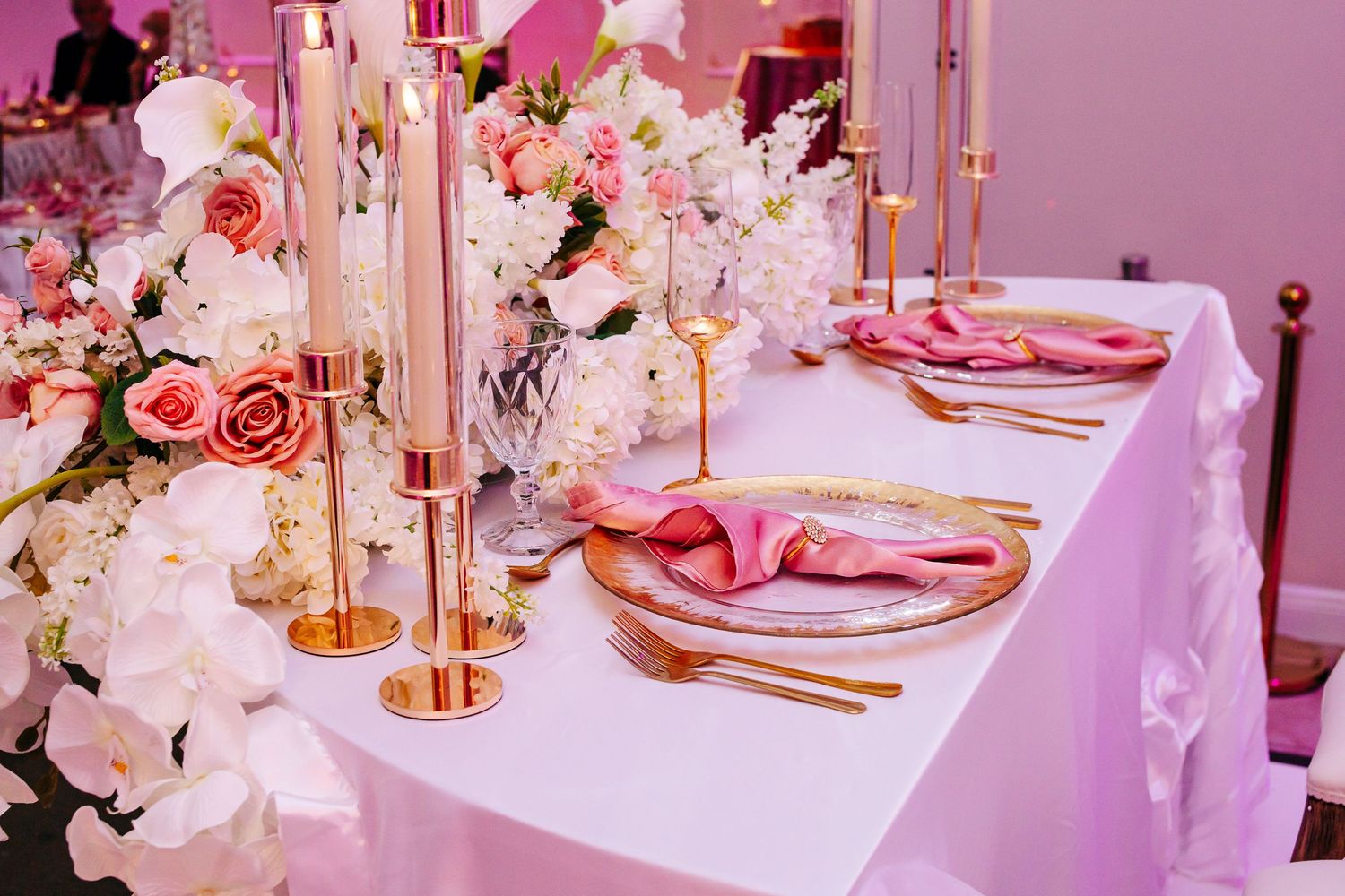 Elegant table setting with pink napkins, gold cutlery, and white floral centerpieces at a formal event.