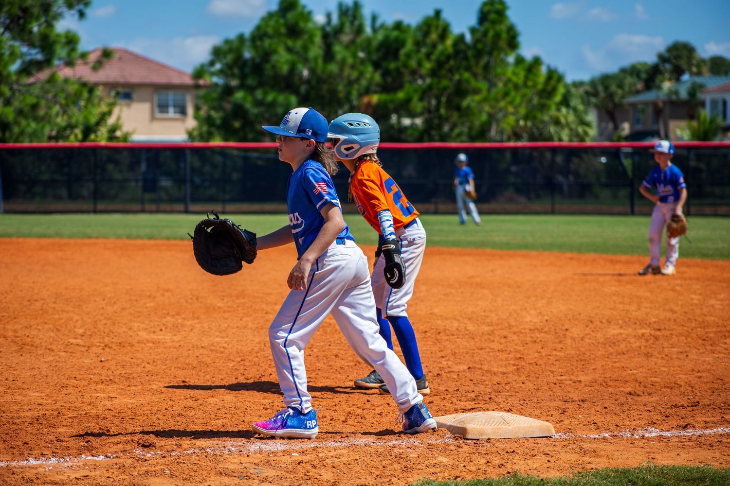 A baseball base runner wearing blue and white jersey slides into first base safely during a game on a dirt field.