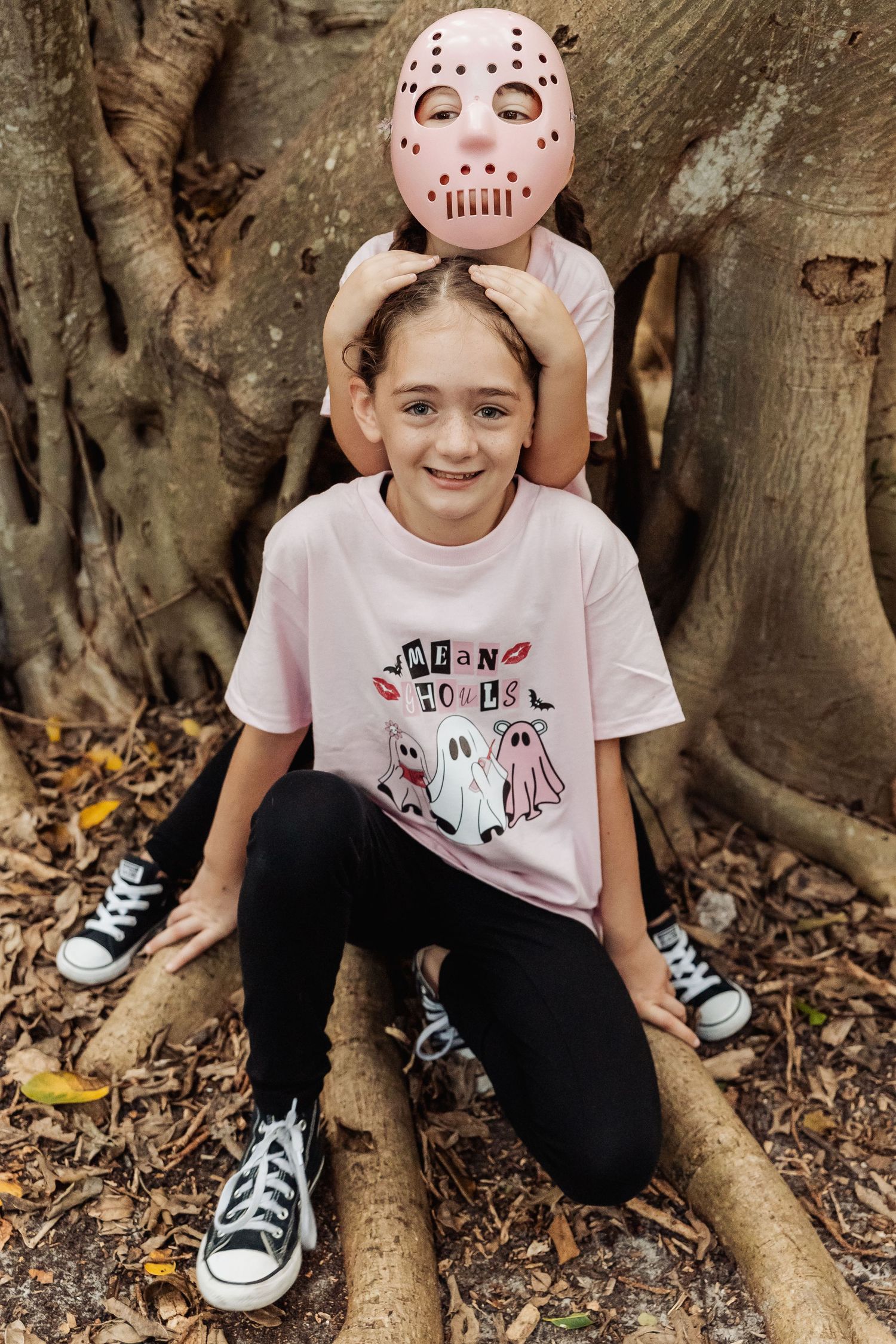 A series of playful photos showing someone sitting on tree roots wearing a Halloween mask and casual clothing.
