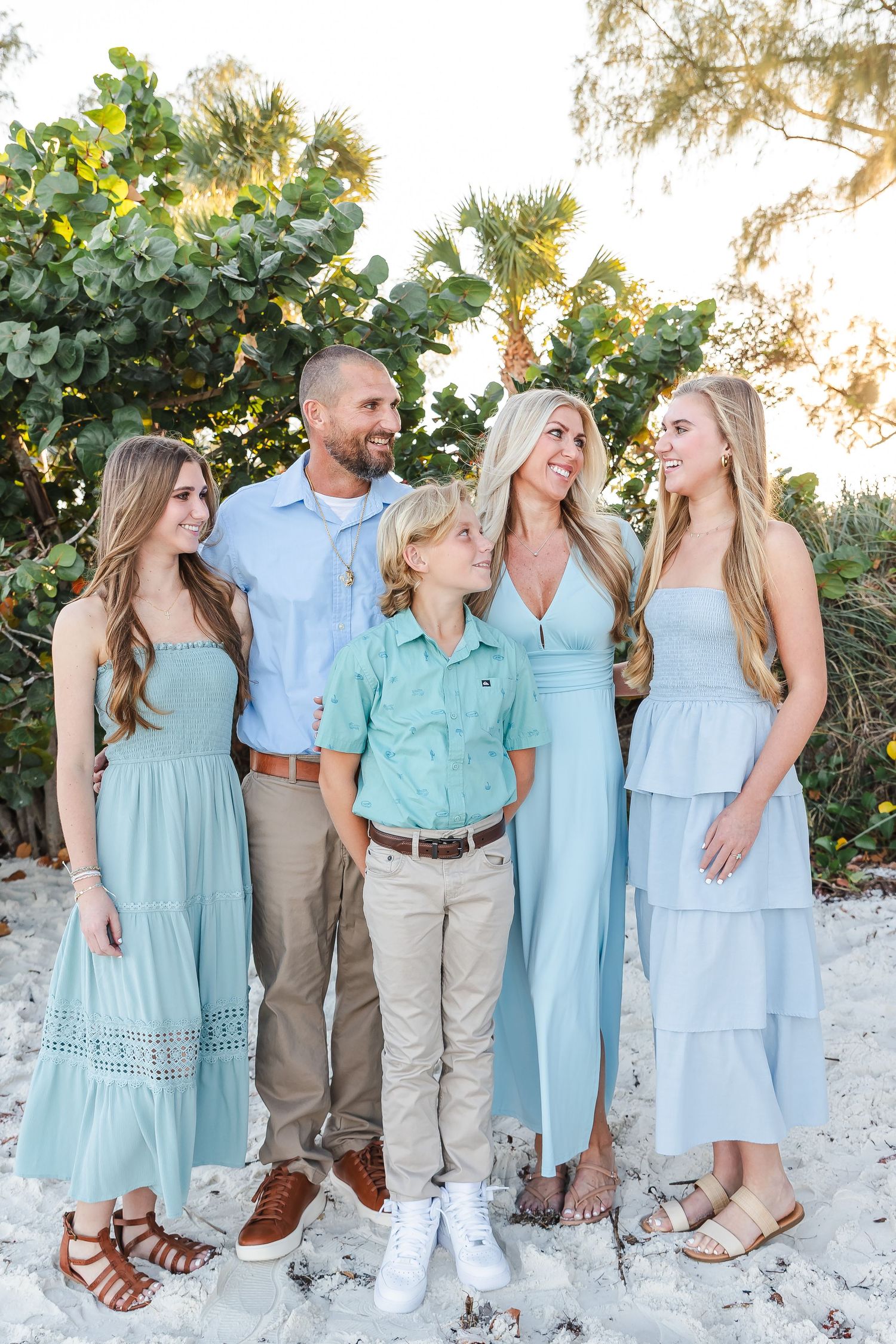 Family group wearing coordinated mint and light blue outfits poses together on a sandy beach.