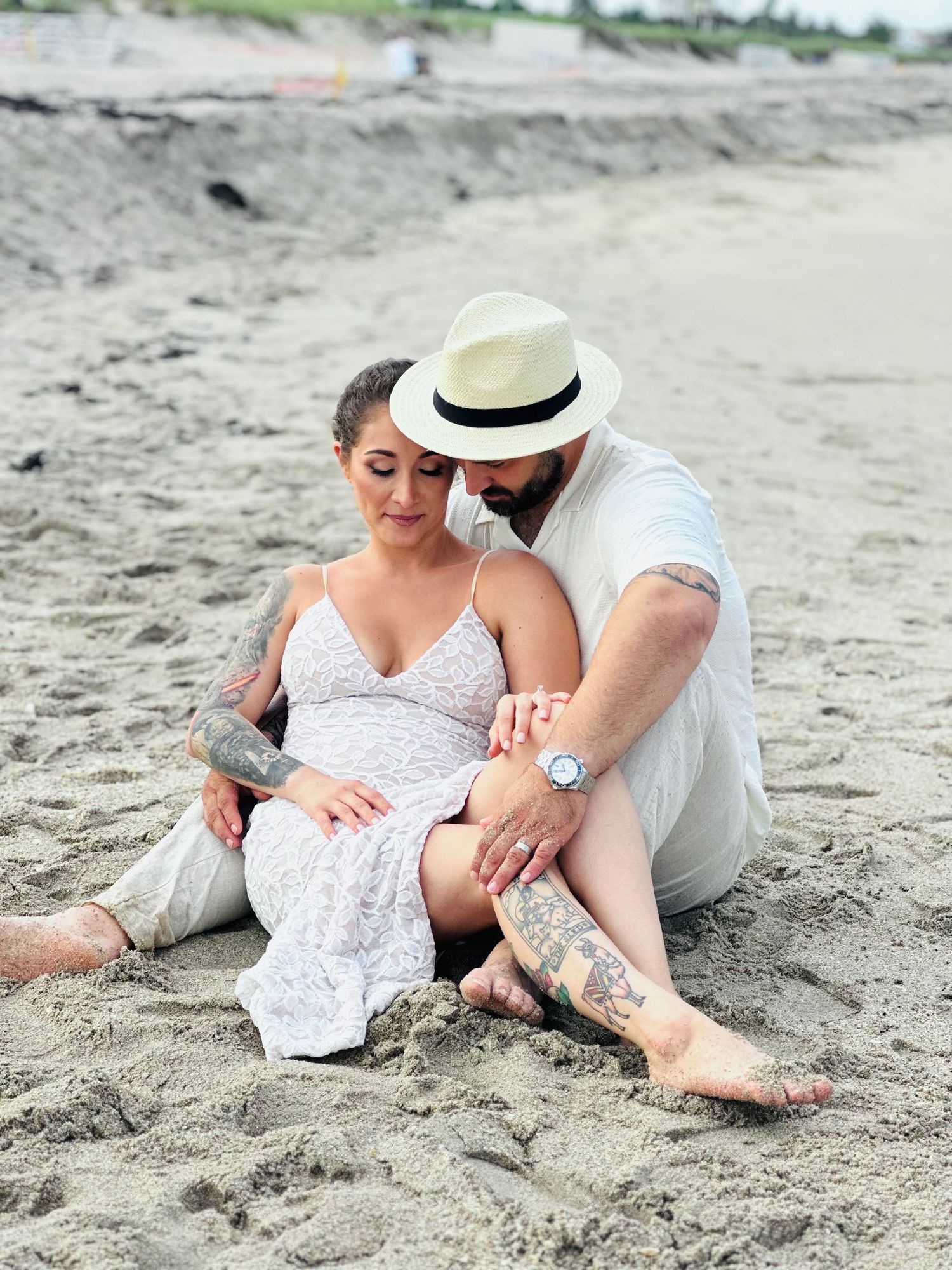Couple in white attire sharing a tender moment on the beach.