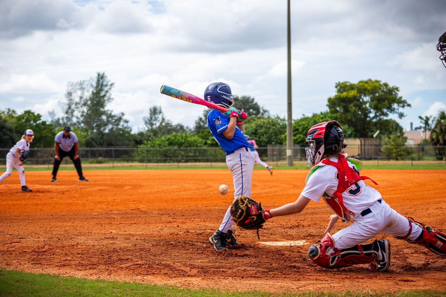 Baseball players engaged in a game on a dirt field with dramatic cloudy skies overhead.