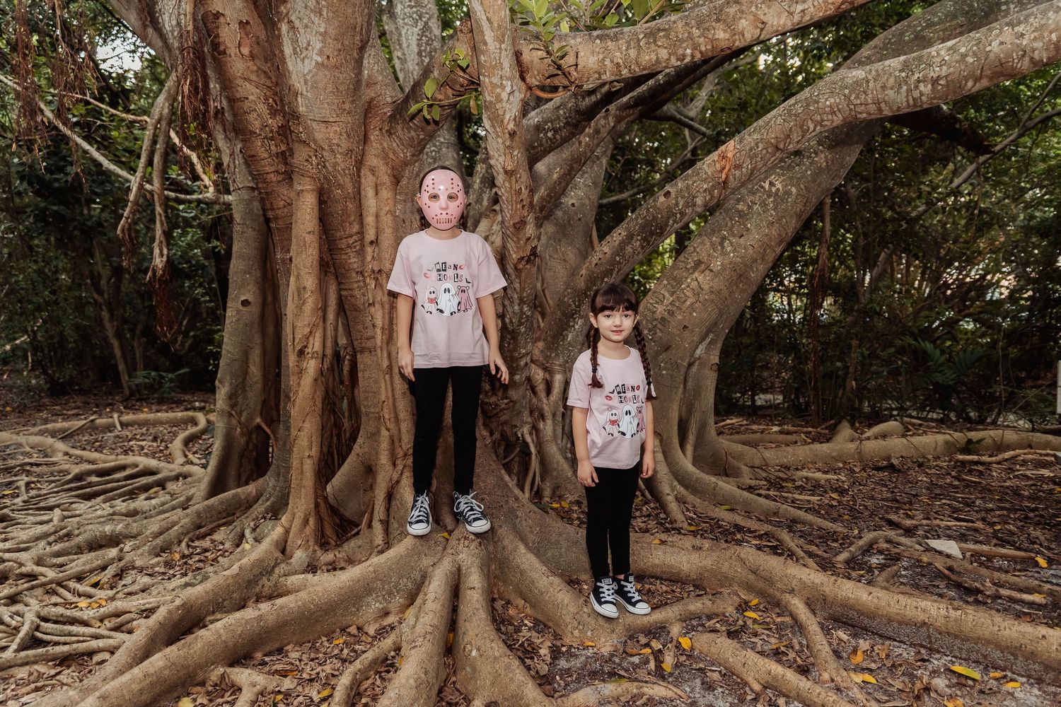 People exploring the massive buttress roots of an ancient Moreton Bay fig tree in a lush forest setting.
