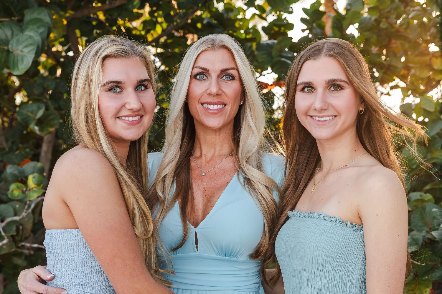 Family members wearing coordinated light blue outfits pose together for outdoor photos at sunset.
